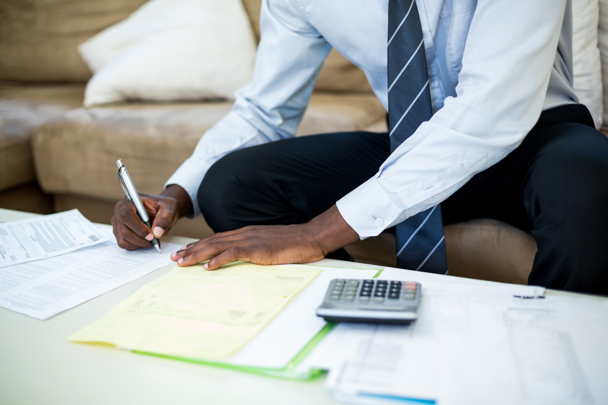 Mid-section of man sitting on sofa and accounting the bills